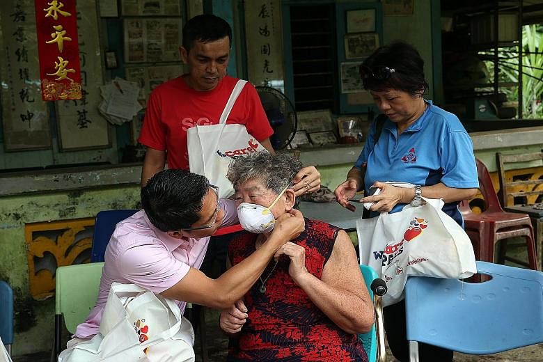 Dr Maliki Osman showing Madam Chen Xiu Zheng, 78, how to wear an N95 mask. Together with volunteers, he gave out WeCare Packs containing masks, eyedrops and other items to residents of Pulau Ubin yesterday. Buildings in the distance shrouded in haze 