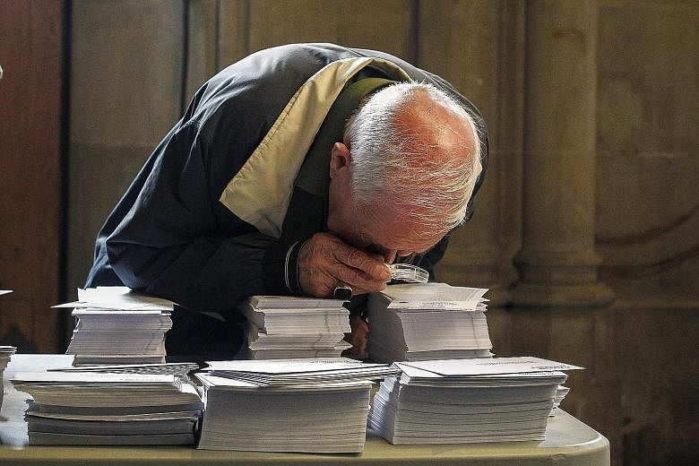 An old man peering at ballot papers in a polling station in Barcelona, Spain, yesterday.