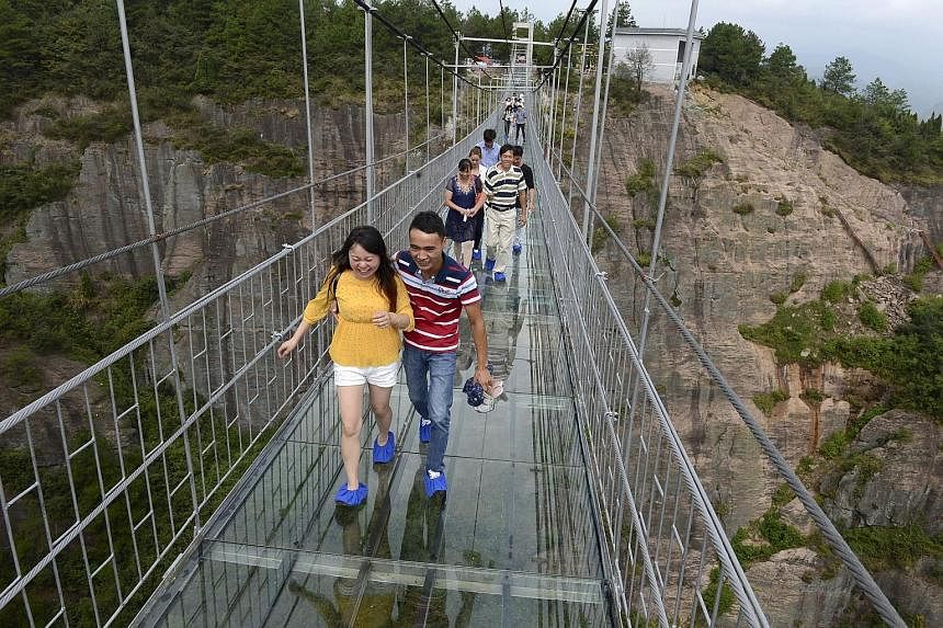 An aerial view of the 300m-long glass suspension bridge (above) at the Shiniuzhai National Geo-park in Hunan province, which opened to tourists (below) for the first time last Thursday.