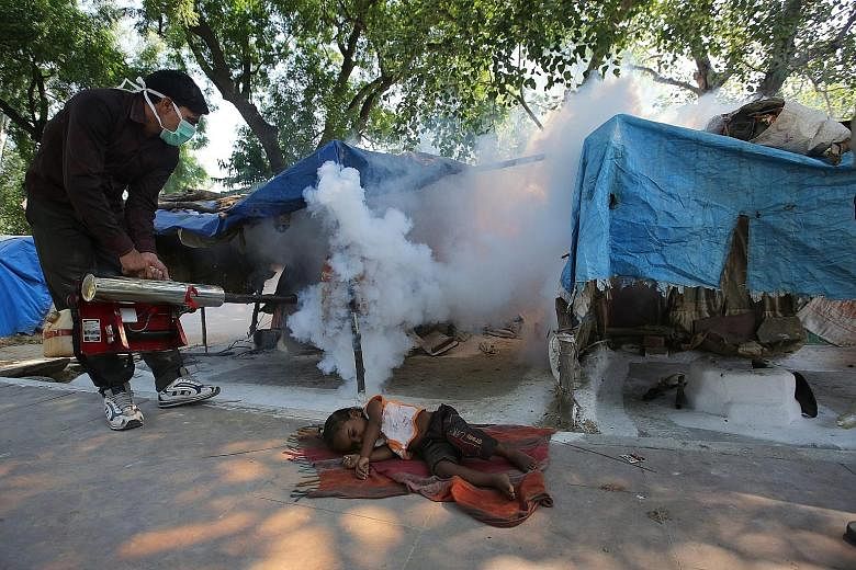 An Indian Municipal Corporation sanitation worker fumigating an area in Old Delhi yesterday, even as a child slept on the ground nearby. The anti-dengue fumigation drive to curb breeding sites for mosquitoes comes amid a dengue outbreak in New Delhi.