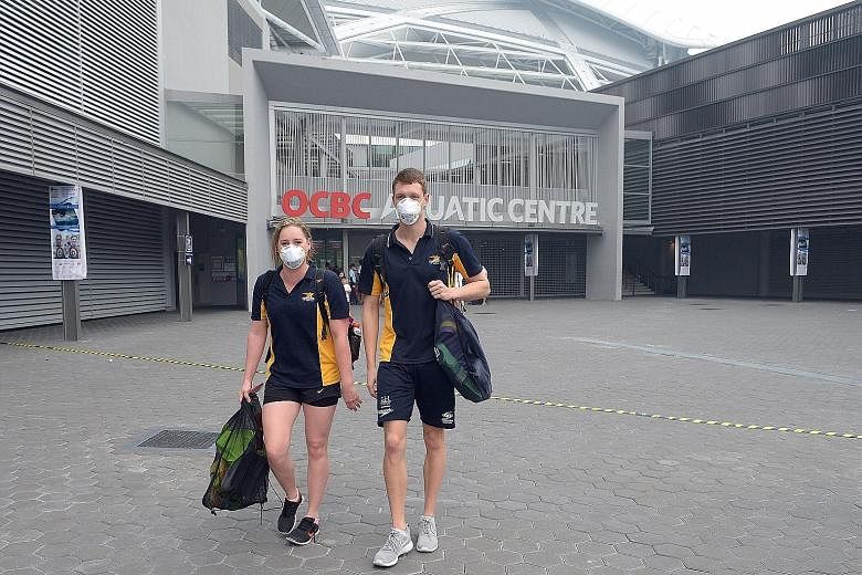 Above: Swimmers Emmabeth Jensen from New Zealand and James McKechnie from Australia leaving the Sports Hub's OCBC Aquatic Centre after the evening finals were cancelled yesterday. The event, which ends today, features over 260 top swimmers from aroun