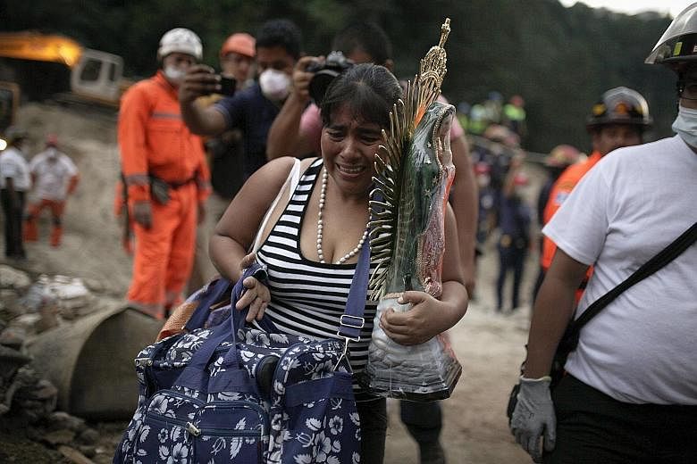 A woman with a religious statue and belongings evacuating from a mudslide-hit area in Santa Catarina Pinula. Hopes of finding more survivors are fading.