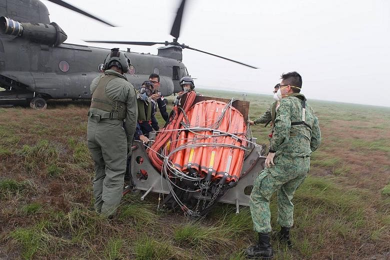 Singapore Armed Forces and Singapore Civil Defence Force personnel moving a heli-bucket into position near a Republic of Singapore Air Force Chinook. A joint water-bombing operation by Indonesia, Singapore and Malaysia kicked off yesterday in South S