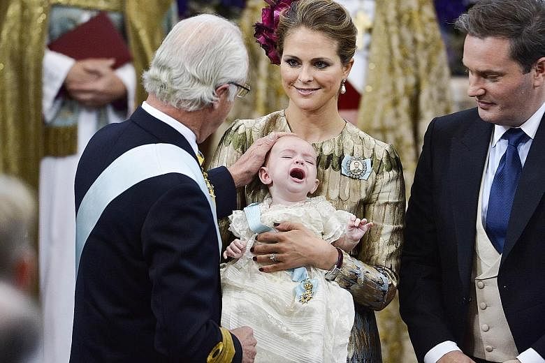 Sweden's King Carl XVI Gustaf touching his grandson Prince Nicolas' head during the baby's christening ceremony at the Drottningholm Palace Church outside Stockholm yesterday. Holding the prince is his mother, Princess Madeleine, and beside them is t