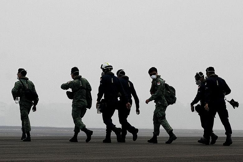 Singapore military and civil defence personnel walking towards a Republic of Singapore Air Force Chinook helicopter at a haze-shrouded airbase in Palembang on Sumatra island yesterday. They were headed for their first aerial water-bombing mission ove