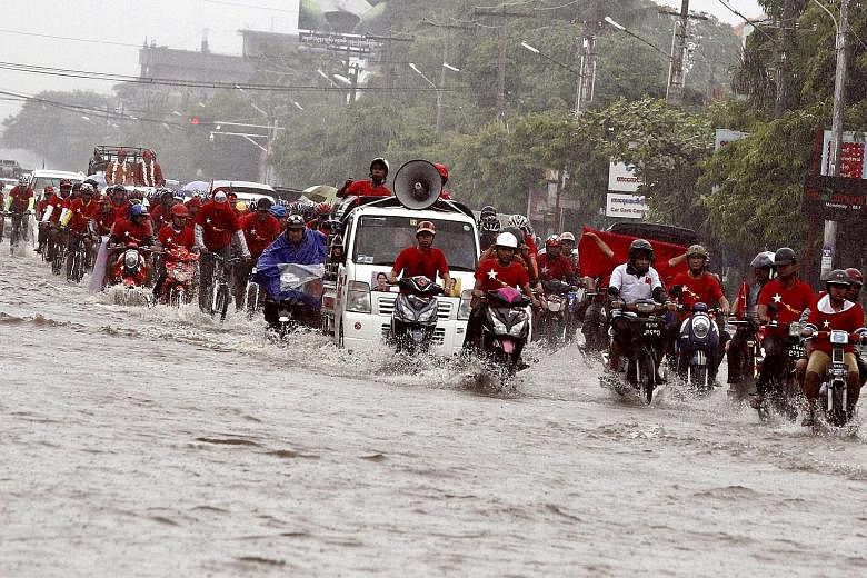 People riding motorbikes and bicycles on a flooded street during a National League for Democracy (NLD) election rally in Mandalay, Myanmar, yesterday. Myanmar's elections will take place as scheduled on Nov 8, state television reported yesterday afte