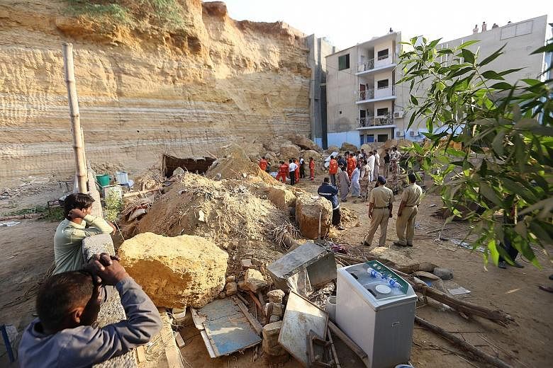 People surveying the debris of a landslide in Karachi, Pakistan, yesterday. At least 13 people were buried alive when their shacks were hit by the landslide, police and rescue workers said, with one victim believed to be as young as six months. Senio