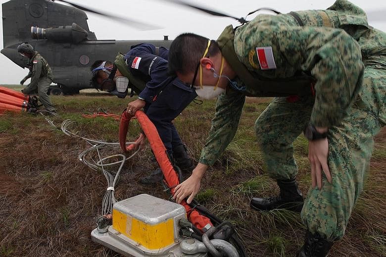 Members of the combined Singapore Armed Forces-Singapore Civil Defence Force firefighting assistance team rigging a 5,000-litre heli-bucket to a CH-47D Chinook helicopter before a water-bombing operation in South Sumatra. The team was deployed to the