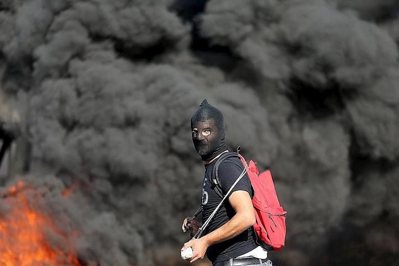 A fire rages behind a Palestinian protester during clashes with Israeli troops near the West Bank city of Ramallah on Wednesday. There has been an upsurge of unrest since Oct 1 and officials have called for Israelis to be vigilant. They also urge hol