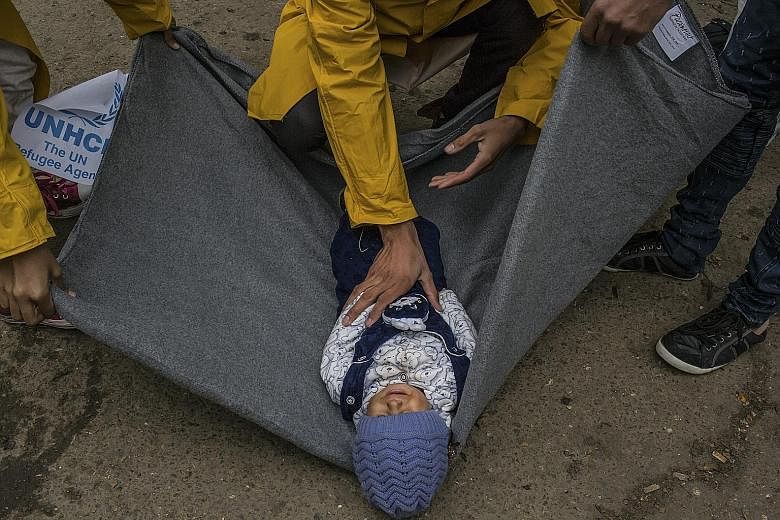 An Afghan man wraps his child in a blanket before crossing into Croatia from Serbia. With autumn winds carrying the first hints of frost, and the situation along European borders unresolved, migrants, aid workers and government officials are anxious 