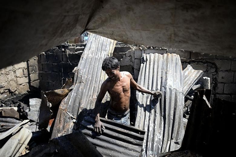 A resident stands among the broken remains of his house, which was gutted after an overnight fire tore through a slum area in Quezon City, Metro Manila, yesterday. The blaze left a scene of devastation in its wake. One hundred houses were destroyed i