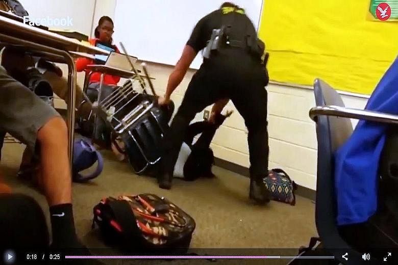 The clip appears to show a white cop putting a black girl in a headlock before flipping her off her chair and dragging her across the floor.