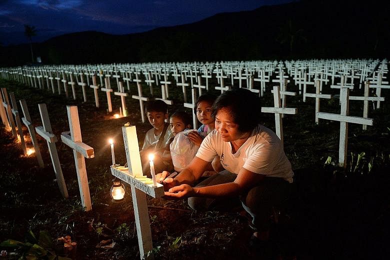 A woman, accompanied by young family members, writing the name of a loved one on a cross at a mass graveyard for the victims of Typhoon Haiyan during All Saints' Day in Tacloban city in the Philippines on Nov 1. Many Tacloban residents are still livi