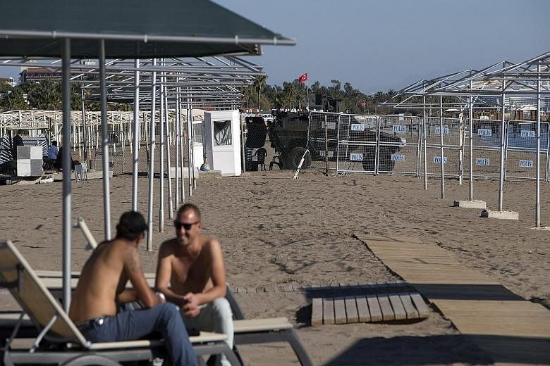 People sitting at the beach in front of barriers to the Group of 20 summit zone in Antalya, Turkey, yesterday. Tourists are not allowed to stay in hotels in Antalya's Belek area over the summit period, and air and sea security systems are in place in