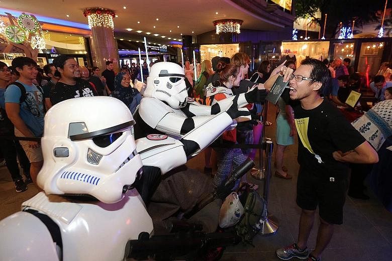 Fans dressed as Star Wars villains Stormtroopers playfully trying to snatch tickets from Mr Nicholas Ho (right).