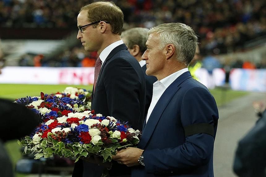 Britain's Prince William and France coach Didier Deschamps carrying floral tributes before the game, in memory of last Friday's Paris terrorist attacks.