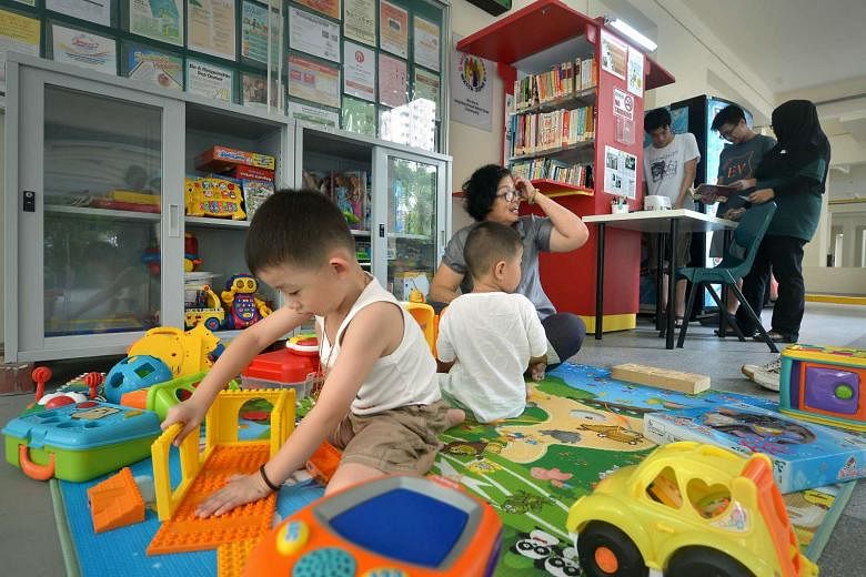 Lee Siang Yu, four, (left) and his brother, Siang Hao, two, with their grandmother, Madam Ho Koon Foong, 61, in the play area of the toy library, while Lim Wee Yang, 16 (standing, in white) and Lai Zi Yang, 16, get help from mobile library assistant Nora 