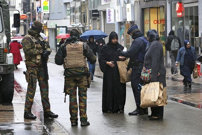 Belgian soldiers patrolling the streets while a police officer checks the documents of a woman shopping in central Brussels yesterday. Belgium raised the alert status for its capital to the highest level yesterday, shutting the metro and warning the 