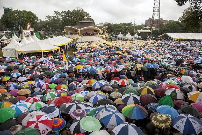 A woman receiving holy communion at a mass led by Pope Francis yesterday. Army personnel conducting security checks on priests. Below: The venue was a sea of umbrellas as people took shelter from the rain before the Pope's arrival.