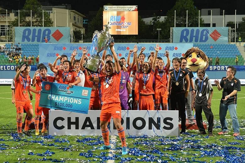 Albirex captain Yosuke Nozawa hoisting the RHB Singapore Cup as players and staff celebrate on the Jalan Besar Stadium pitch. The Japanese side finished third in the S-League, equalling their best result.