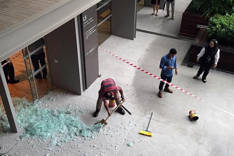The shattered glass door (left) on Level 5 of the National Gallery, and workers (above) putting up a screen in the area yesterday. A man suffered minor abrasions on his right hand in the incident.