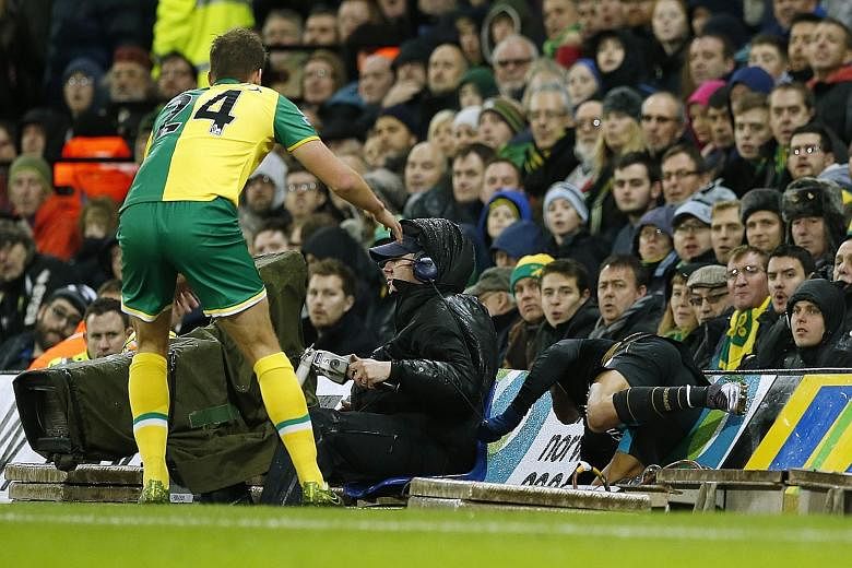 Arsenal's Alexis Sanchez crashes into the advertising boards as Norwich's Ryan Bennett looks on. The Gunners are hoping that Sanchez has pulled his hamstring instead of tearing it, as this will involve a quicker recovery.