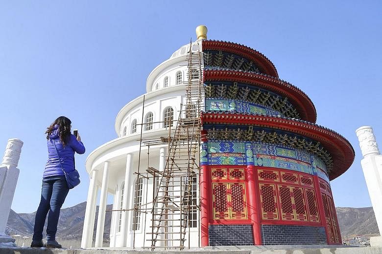 A woman taking photos of a building at a film and television production studio on the outskirts of Shijiazhuang, the capital of Hebei province in northern China. Half the building is a replica of the Qinian Hall in the Temple of Heaven (right), a pop