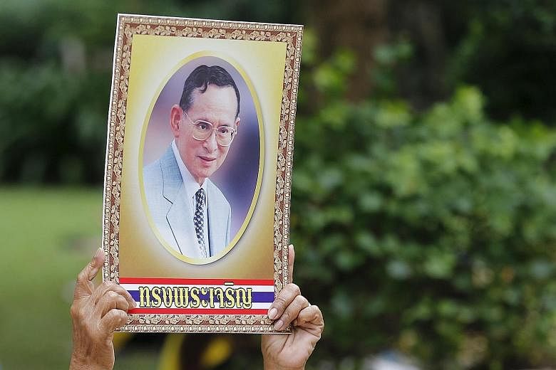 A supporter holding a portrait of King Bhumibol Adulyadej outside Siriraj Hospital in Bangkok yesterday, where a few hundred people gathered to mark his birthday. The words on the portrait read "Long live the King!"