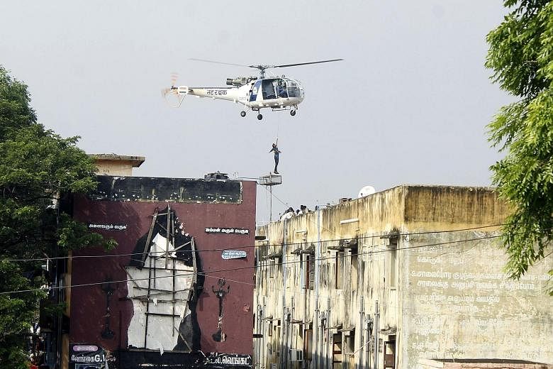 An Indian rescue helicopter lifting a man off a roof of apartment buildings surrounded by floodwaters in Chennai on Friday. Thousands of rescuers are racing to evacuate victims of flooding in Tamil Nadu.