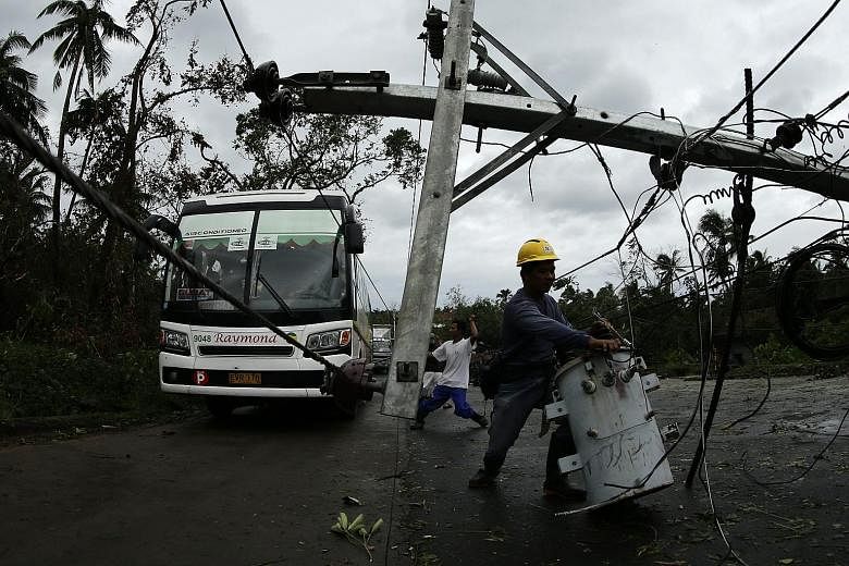 Above: Residents surveying the damage wrought by Typhoon Melor yesterday after it battered the town of Barcelona, in Sorsogon province in the central Philippines. Right: Workers clearing a fallen electric post in Castilla, Sorsogon province. Cold nor