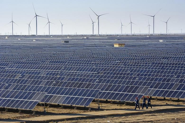 While wind and sunshine are free, wind turbines and solar panels, like these at a power plant in Xinjiang, China, are not. Fossil fuels are also needed to build these facilities and produce solar cells, says the writer.