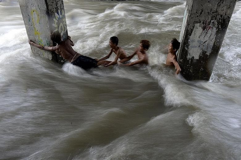 Children swimming in a creek swollen with floodwaters in Manila yesterday. The storm, known locally as Onyok, weakened into a low pressure area after hitting land late on Friday, but continued to bring more rain to Mindanao and the central Visayas is