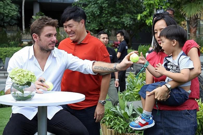 Tennis world No. 4 Stan Wawrinka handing three-year-old Caleb Lau an autographed ball at OUE Twin Peaks yesterday morning. The Swiss two-time Grand Slam champion, who is in town as the marquee player for the OUE Singapore Slammers, spent time meeting