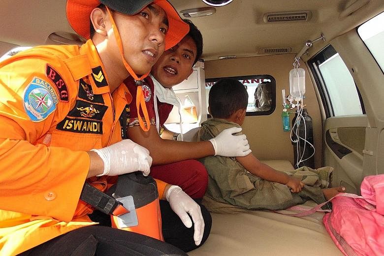 Two members of a search-and- rescue team with a young survivor in Siwa. The vessel was ferrying 118 people around Sulawesi island when it sent out a distress signal last Saturday afternoon.