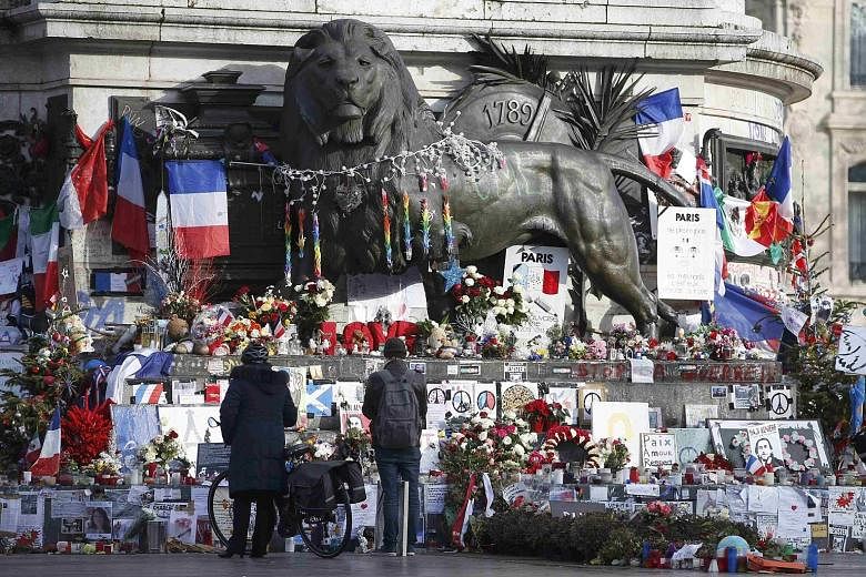 People looking at flowers and messages at the Place de la Republique in Paris paying tribute to the victims of the Charlie Hebdo attack last January and the coordinated attacks in the French capital last November. The commemorative issue of the magaz