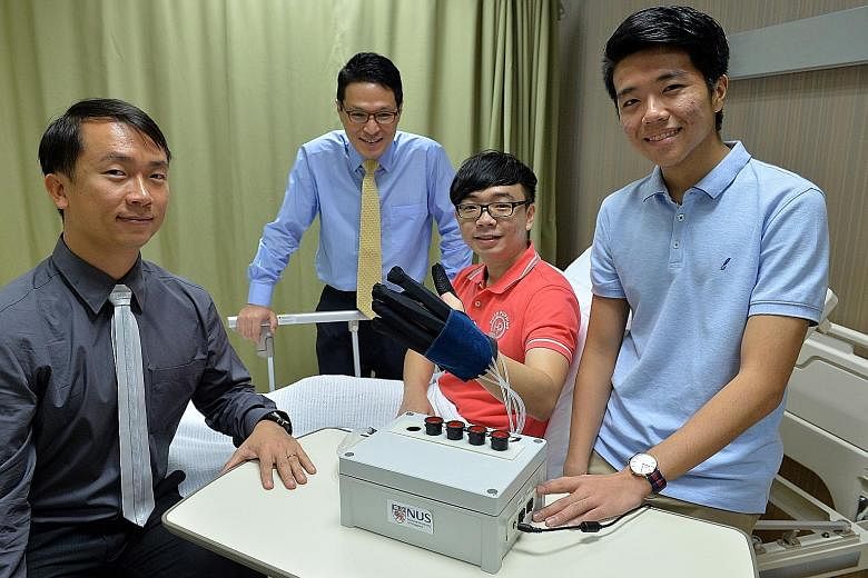 Far left: The team from NUS' biomedical engineering unit include (from left) Prof Yeow, Assistant Professor Lim Jeong Hoon, Mr Yap Hong Kai and Mr Benjamin Ang Wee Keong Left: Mr Yap demonstrating how the robotic glove helps patients to carry out reh