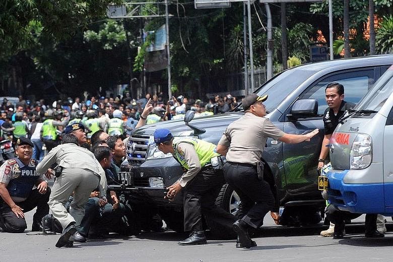 Indonesian police officers taking cover behind a vehicle during an exchange of gunfire with militants, after a series of blasts in downtown Jakarta yesterday.