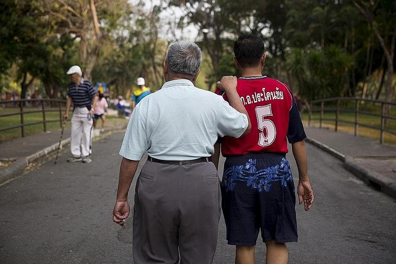An elderly man holding another man's shoulder while walking through Lumpini Park in Bangkok. Households headed by the elderly are twice as likely to be poor as those headed by people in their 30s and 40s.