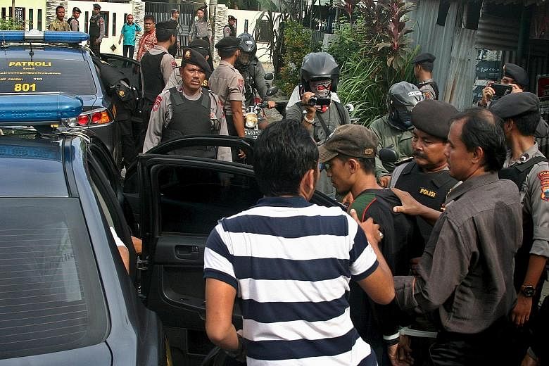 Anti-terror police (top) with evidence taken from the house of a suspected militant involved in Thursday's attack in Jakarta. Indonesian police (above) with a man (in cap) arrested during a raid in Java on Friday. So far, 12 people have been arrested