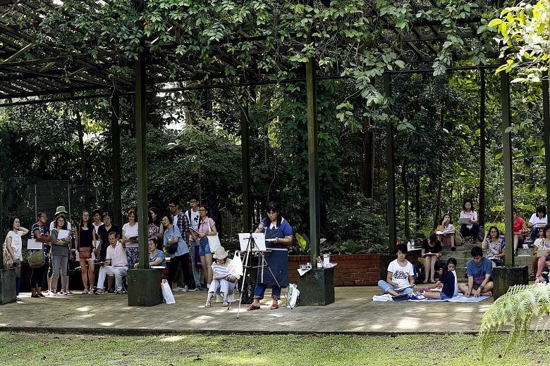 Mr Tham Pui San holding up a painting (left photo) and surrounded by participants (right photo) at the Singapore Botanic Gardens. The free sessions last two or three hours.