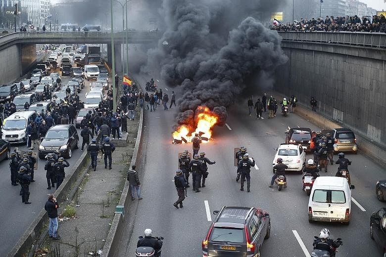 Anti-riot policemen dispersing taxi drivers and putting out burning tyres (above) on the ringroad around Paris yesterday. The taxi drivers also blocked traffic (below) in other parts of France as part of a national protest against competition from pr