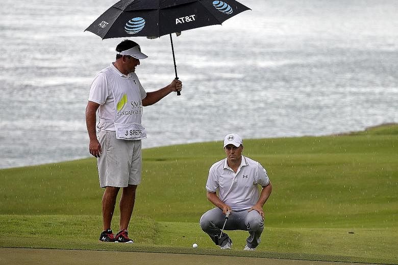 Jordan Spieth taking shelter from the rain under the umbrella of manager and stand-in caddie Jay Danzi at the SMBC Singapore Open yesterday. After a fine opening 67, he was even par after six holes when play was called off. He and 77 others will resu