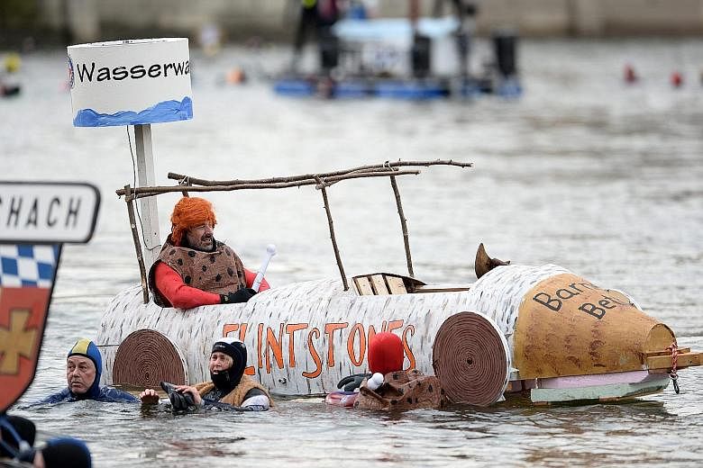 A participant (left) dressed as Fred Flintstone, the lead character in the TV cartoon The Flintstones, sitting in a handmade boat on the Danube river, while other costumed swimmers (above) wave to spectators during the 47th Donauschwimmen (Danube Swi