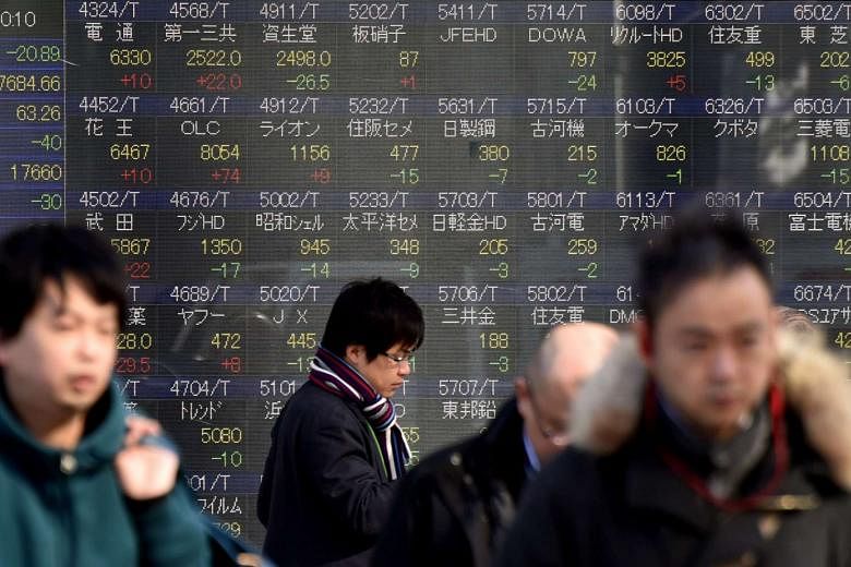 Pedestrians walk past a stock prices board showing figures from the Tokyo Stock Exchange on Feb 2, 2016.