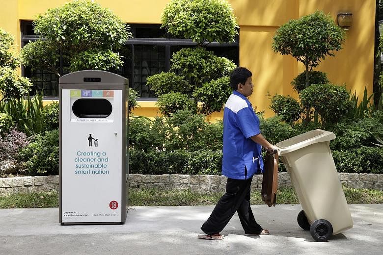 Madam Jamaliyah wheeling a normal bin away from the smart bin, which has a compactor and can store up to eight times more rubbish than a normal bin of the same size.