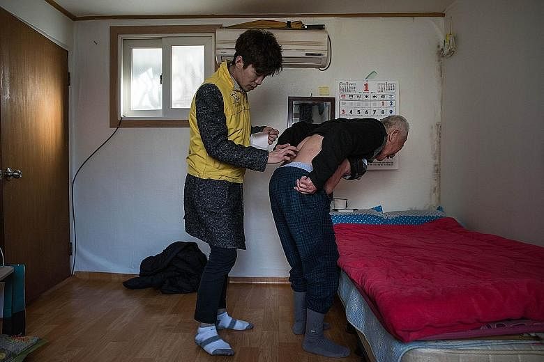 An elderly South Korean getting some help applying a heating pad in his one-room flat in Seoul. A new report says the number of single-person households in South Korea last year was about 5.06 million, a 7.7-fold surge from 661,000 in 1985.