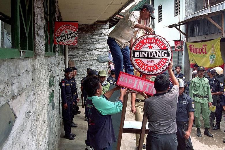 Government workers removing a beer advertisement in front of a brothel in the Kalijodo red-light district. The Jakarta administration is pushing forward with a plan to clean up the area and relocate some 300 residents.