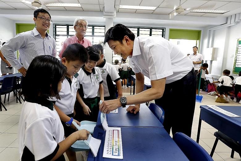 Acting Minister for Education (Schools) Ng Chee Meng (far right) lending a hand to pupils in Xingnan Primary School as they cleaned their classroom yesterday, with Public Hygiene Council chairman Edward D'Silva (in pink shirt) and school principal Ch