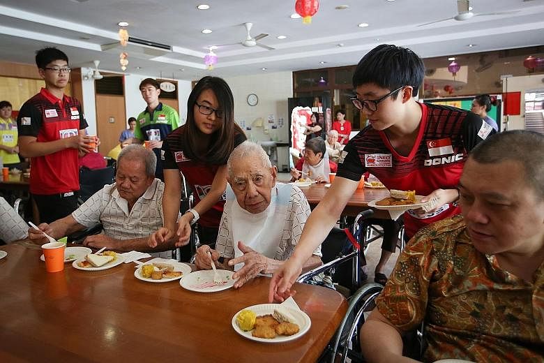 Singapore's women's table tennis players Feng Tianwei (right) and Isabelle Li serving food to elderly residents at the Man Fut Tong Nursing Home on the team's visit there yesterday. The women have set themselves a target to win a medal at the World T