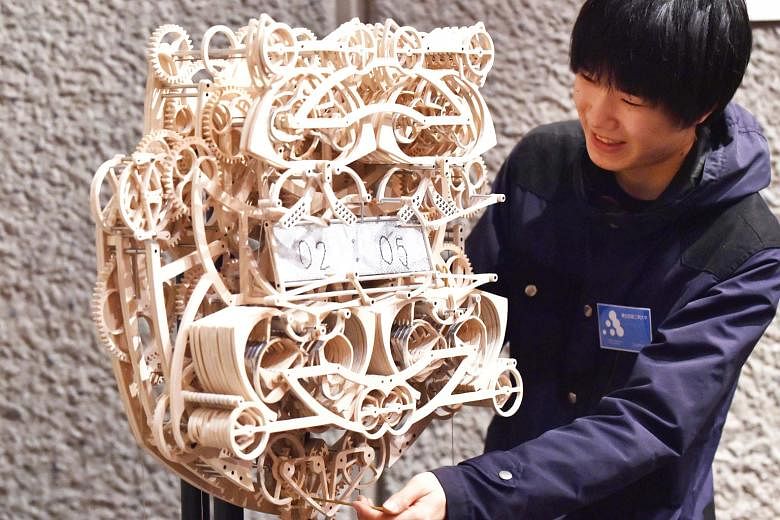 Japan's Tohoku University of Art and Design student Suzuki Kango, 22, with his wooden clock at the Tokyo Metropolitan Art Museum. The 407-piece clock took him six months to build and is set into motion by a series of weights. It writes the time on a 
